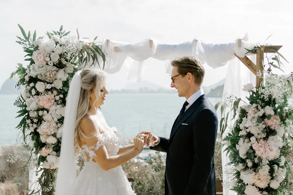 Los novios intercambiando los anillos bajo el arco, con el mar detrás